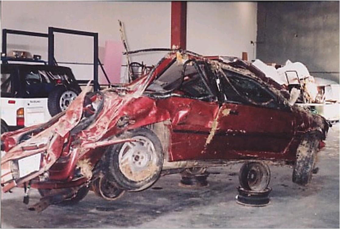 Kevin's car after the crash of 24 June 2000, the front end and roof destroyed, propped on bare wheel rims in a storage warehouse