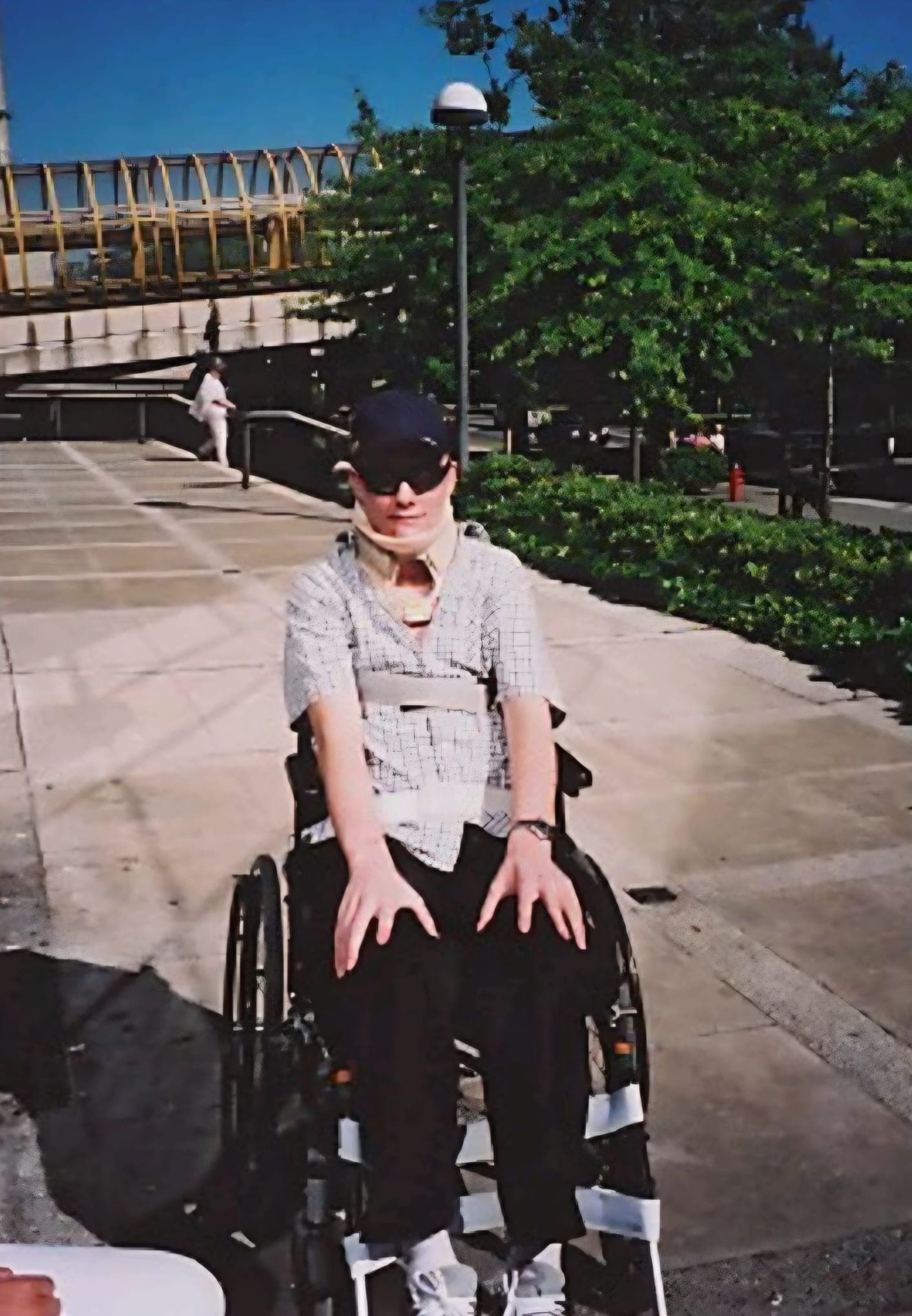 Kevin outside in the sun not long after the crash, in a wheelchair and a neck brace, hands resting on his knees