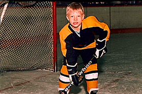 Kevin as a young boy in full hockey gear, standing in front of a net