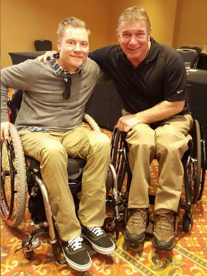 Kevin side by side with Rick Hansen, both in wheelchairs at a conference