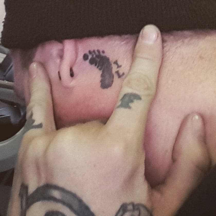 Two small footprints tattooed on Kevin's forearm beside a semi-colon.